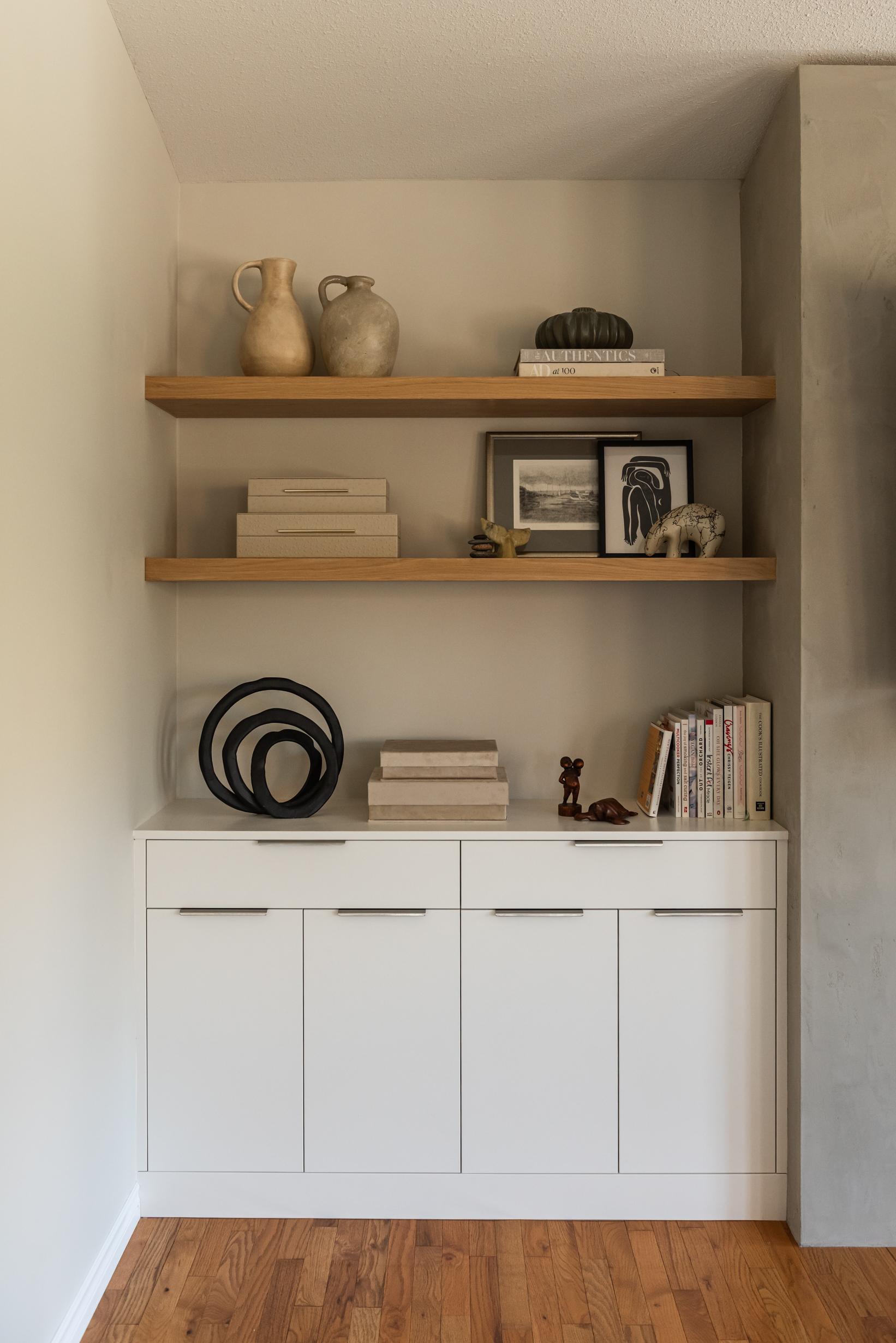 Custom living room built ins with closed cabinetry for storage and white oak open shelving styled with art and decor.
