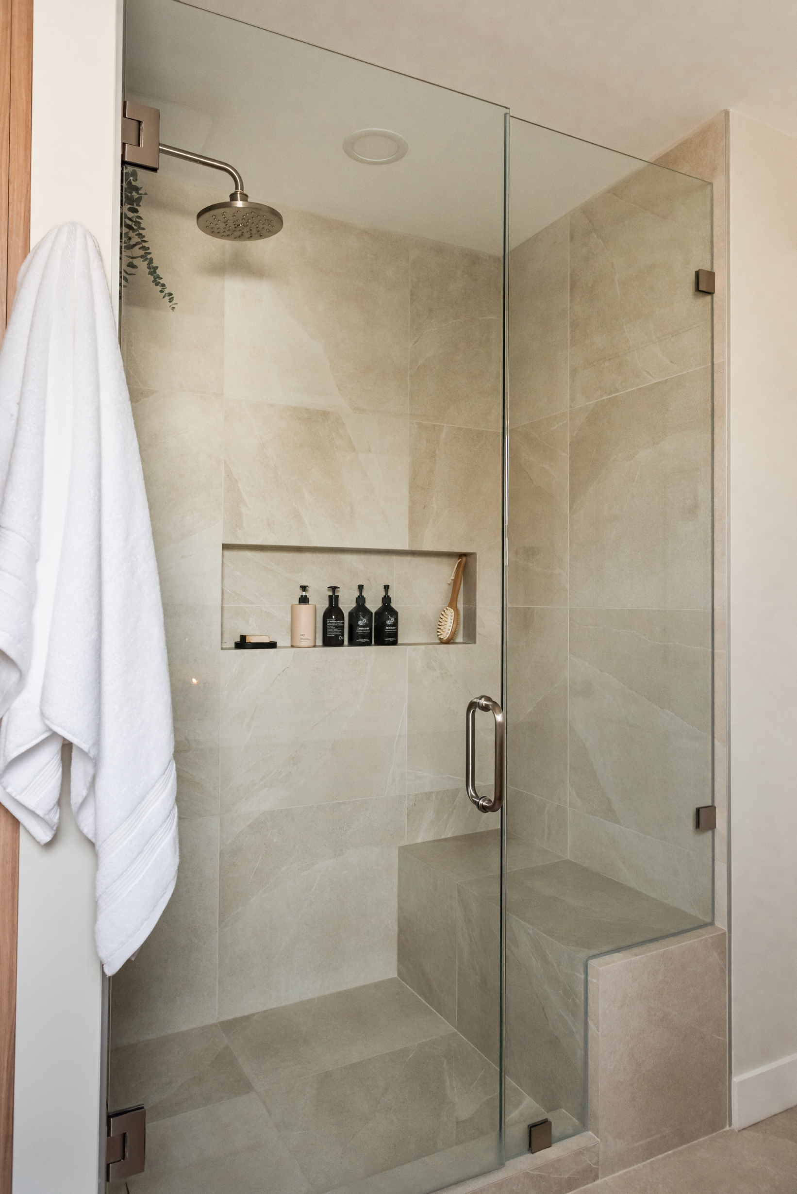 Ensuite bathroom featuring large tiled walk in shower with built in bench, oversized niche, and rainfall shower head.