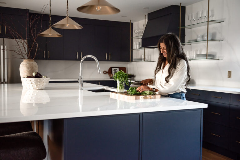 Women in bright renovated kitchen with large island, navy blue cabinetry, and warm wood accents in a family-focused home renovation