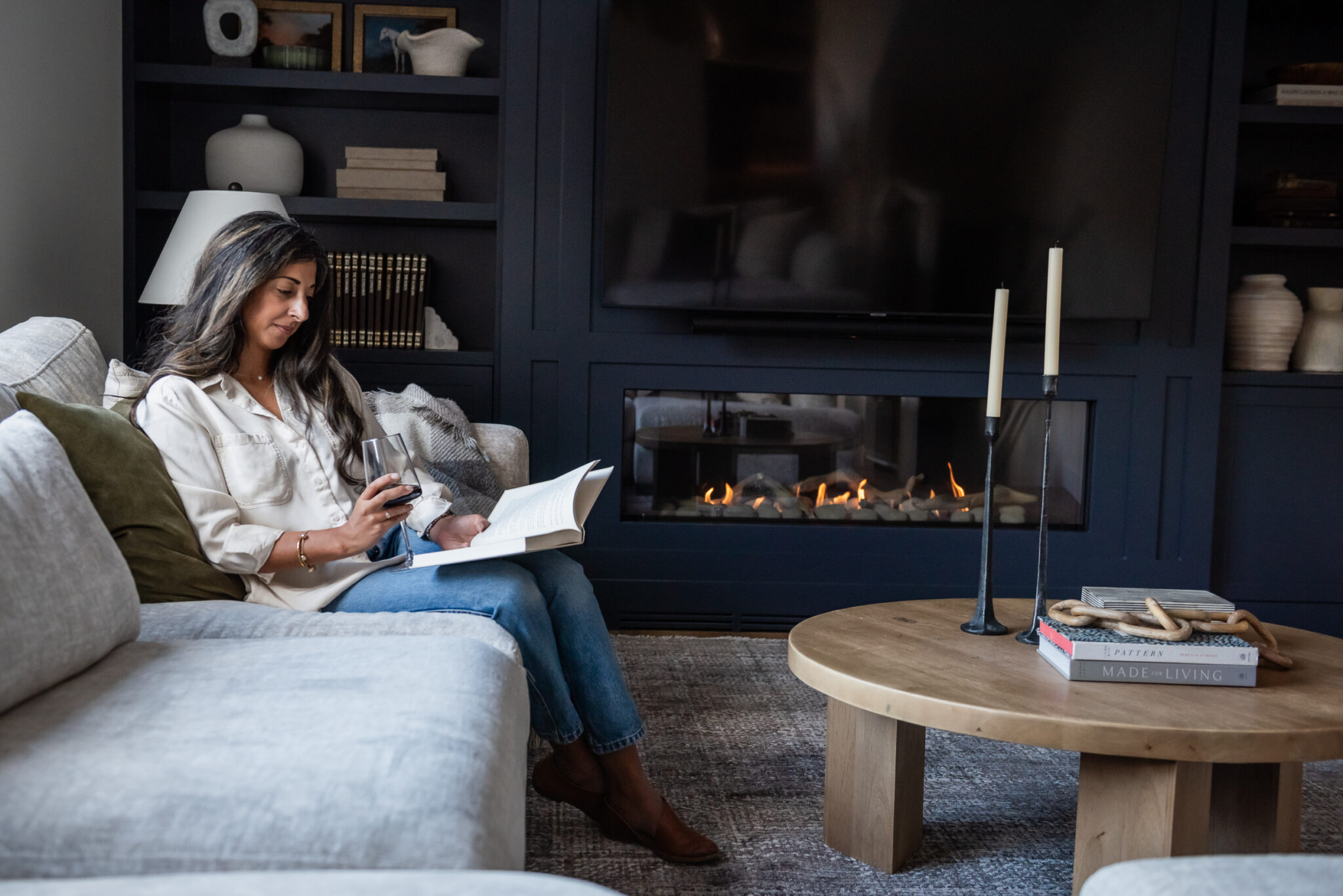Woman decorating built in cabinetry in modern living room with linear fireplace