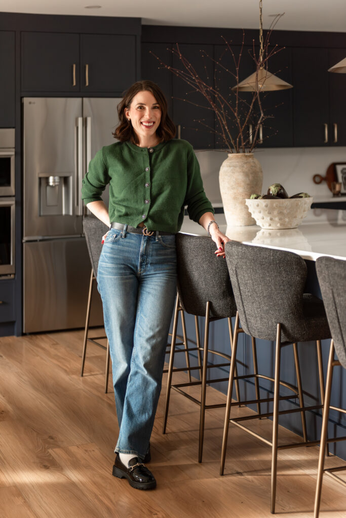 Woman in bright renovated kitchen with large island, navy blue cabinetry, and warm wood accents in a family-focused home renovation