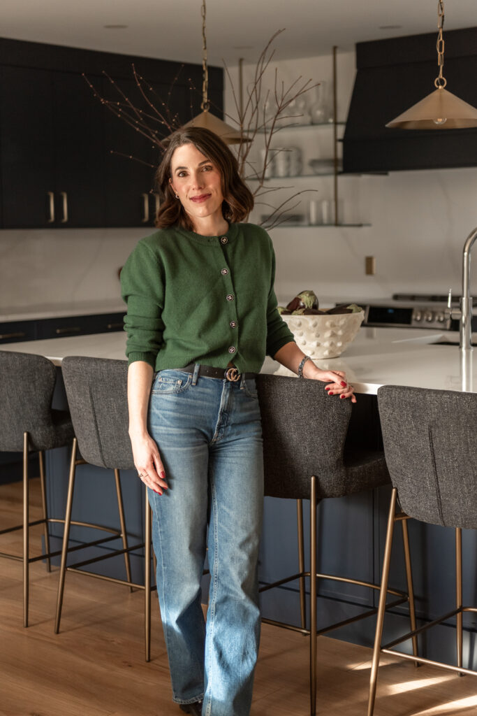 Woman in bright renovated kitchen with large island, navy blue cabinetry, and warm wood accents in a family-focused home renovation