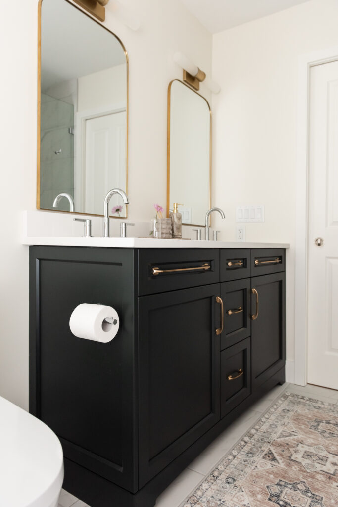 Renovated primary ensuite with deep hunter green vanity, freestanding tub, and brass lighting