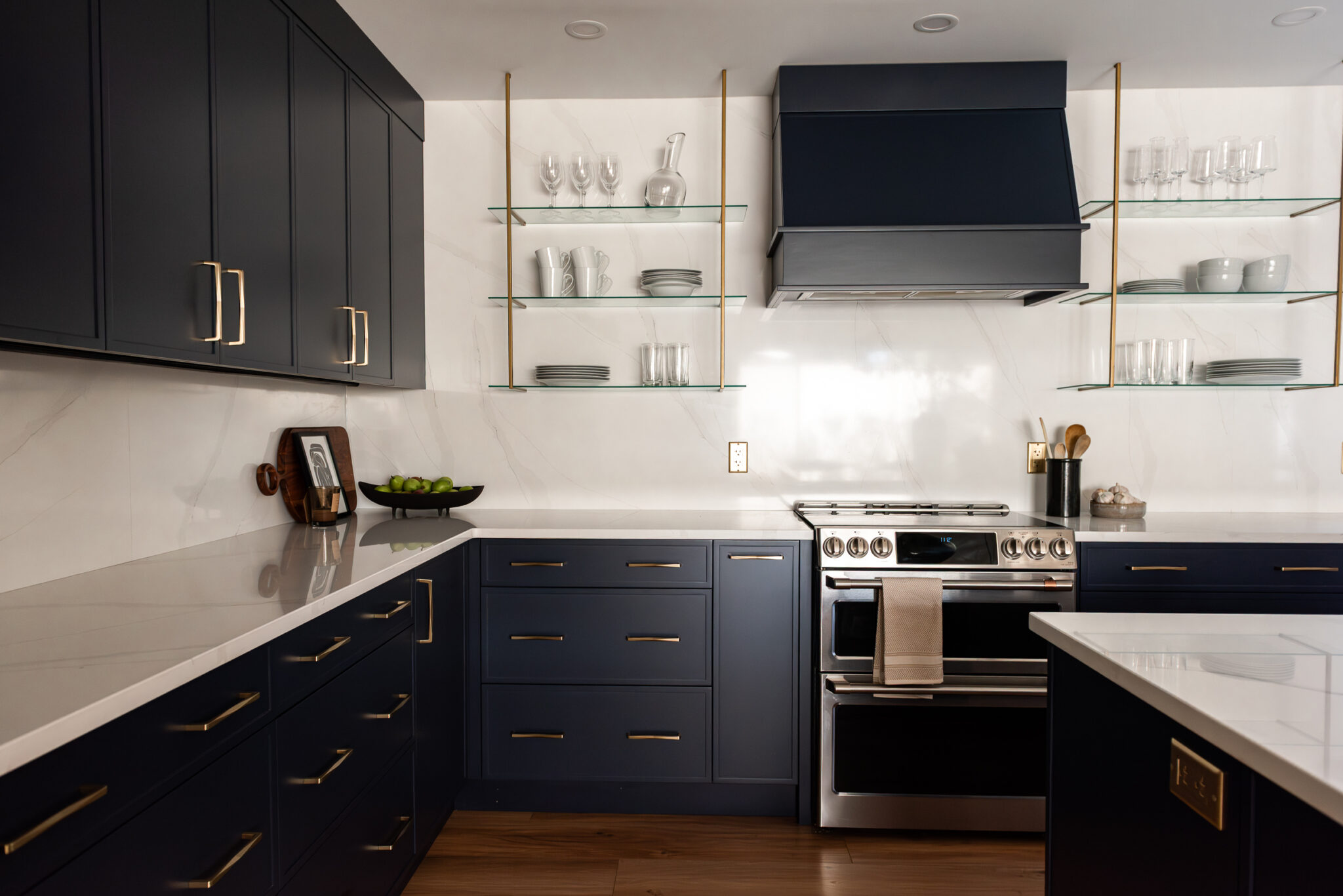 Modern kitchen range wall with navy cabinetry, statement hood, tile backsplash, and wood shelving