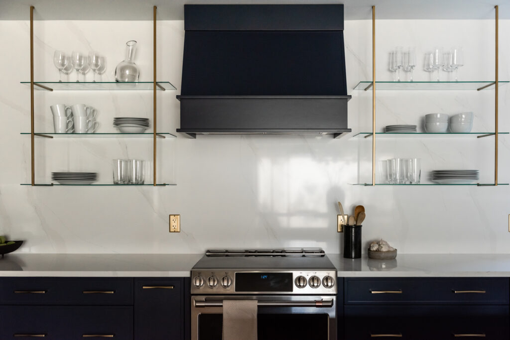 Modern kitchen range wall with navy cabinetry, statement hood, tile backsplash, and wood shelving