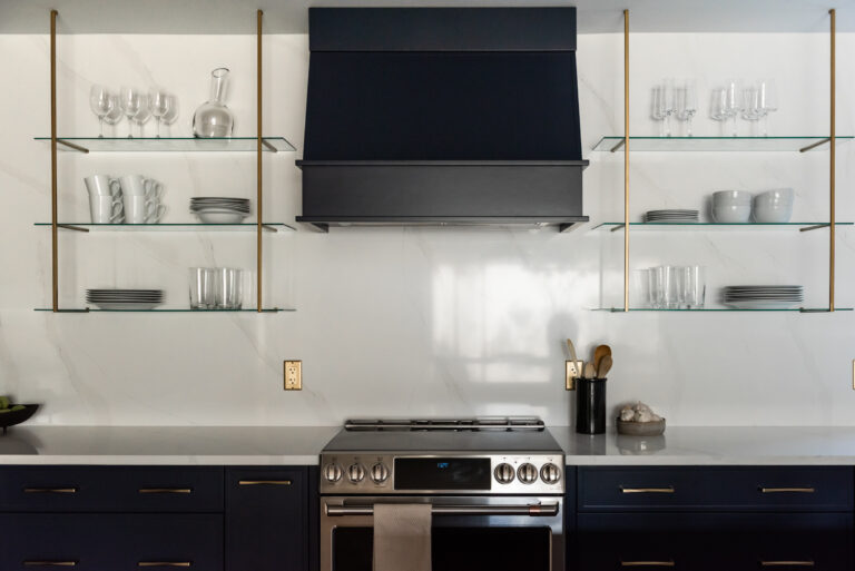Modern kitchen range wall with navy cabinetry, statement hood, tile backsplash, and wood shelving