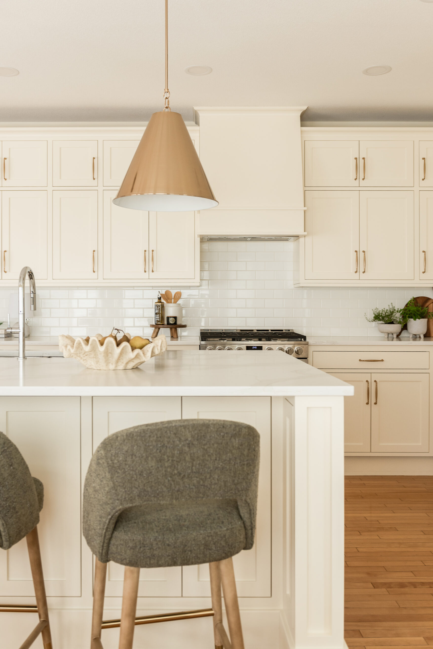 Custom range hood and white subway tile backsplash framed by restored inset cabinetry in a classic cream kitchen renovation.