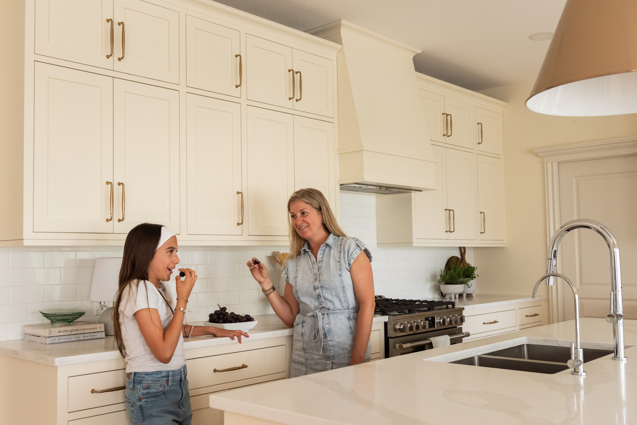 Family enjoying a renovated cream kitchen with preserved inset cabinetry, white quartz counters, brass hardware, and warm maple floors in this Vinecrest home renovation.