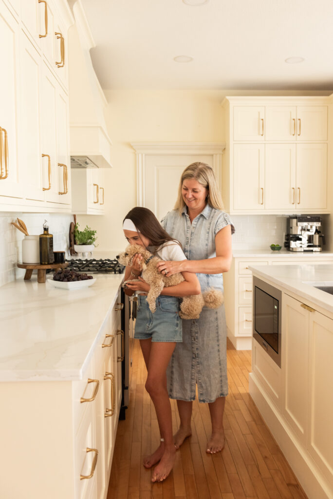 Family enjoying a renovated cream kitchen with preserved inset cabinetry, white quartz counters, brass hardware, and warm maple floors in this Vinecrest home renovation.