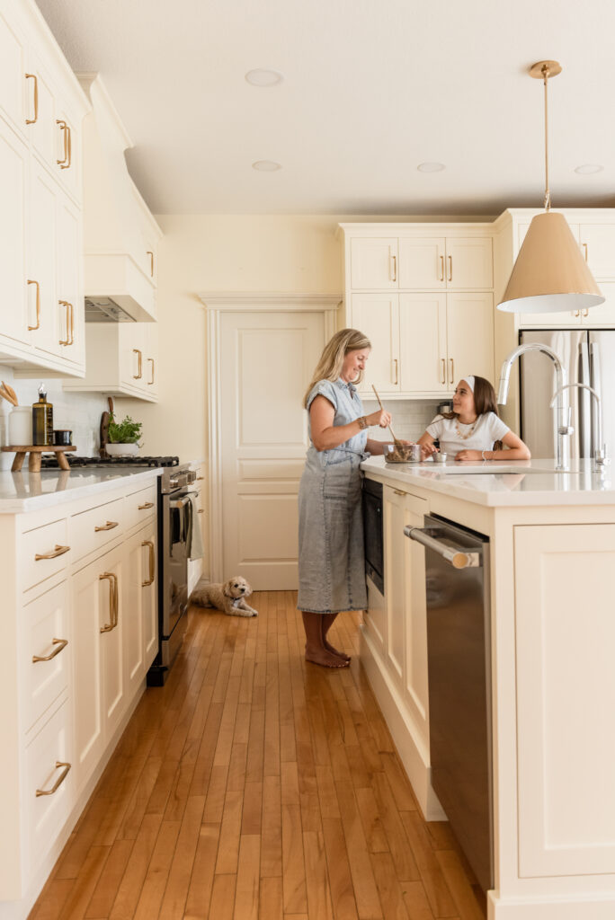 Family baking in a timeless cream kitchen renovation featuring restored craftsman cabinetry, white quartz countertops, brass hardware, and improved island functionality.