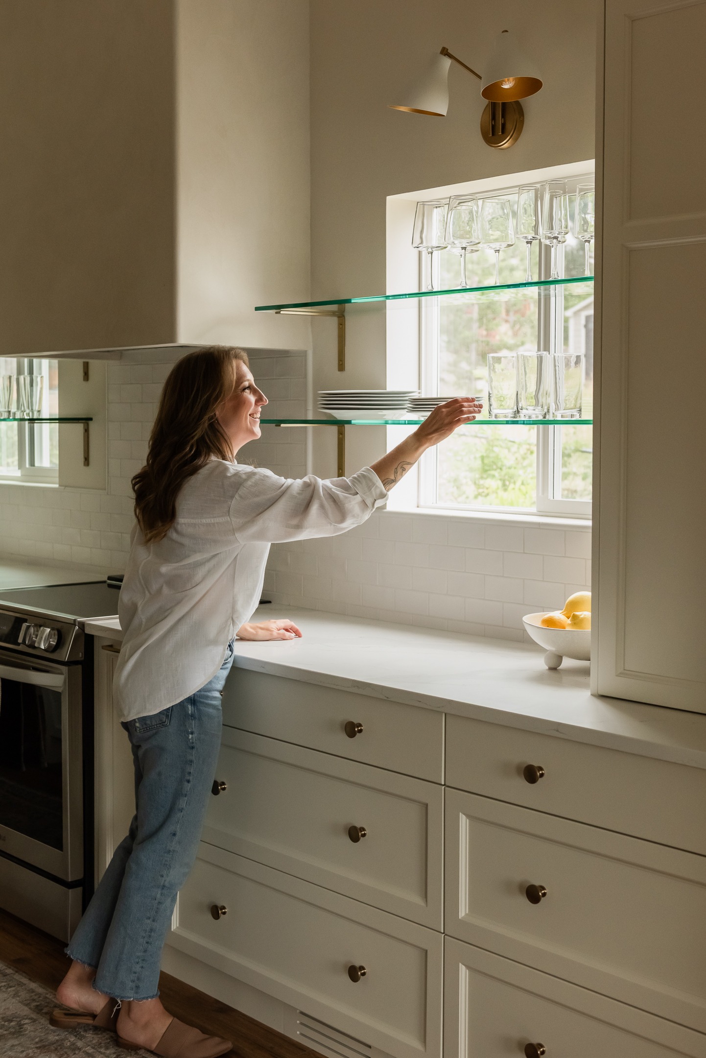 Woman reaching for dishes on glass shelf in front of window in newly renovated Kelowna kitchen