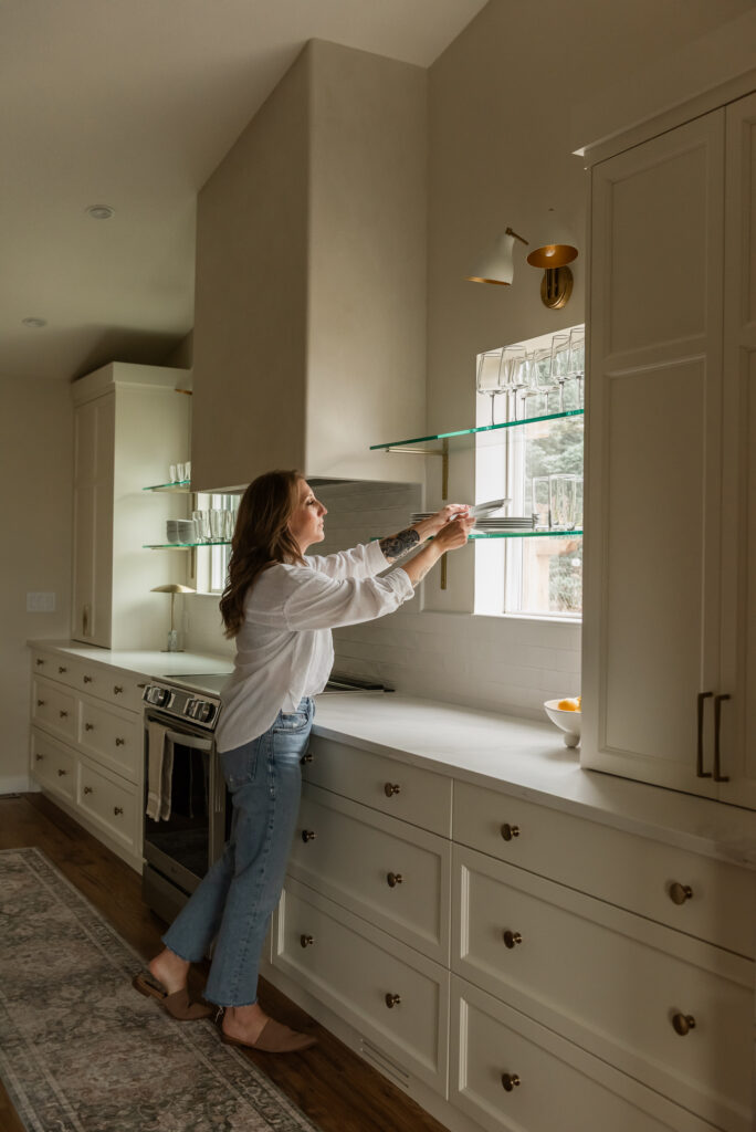 Woman reaching for dishes on glass shelf in front of window in newly renovated Kelowna kitchen