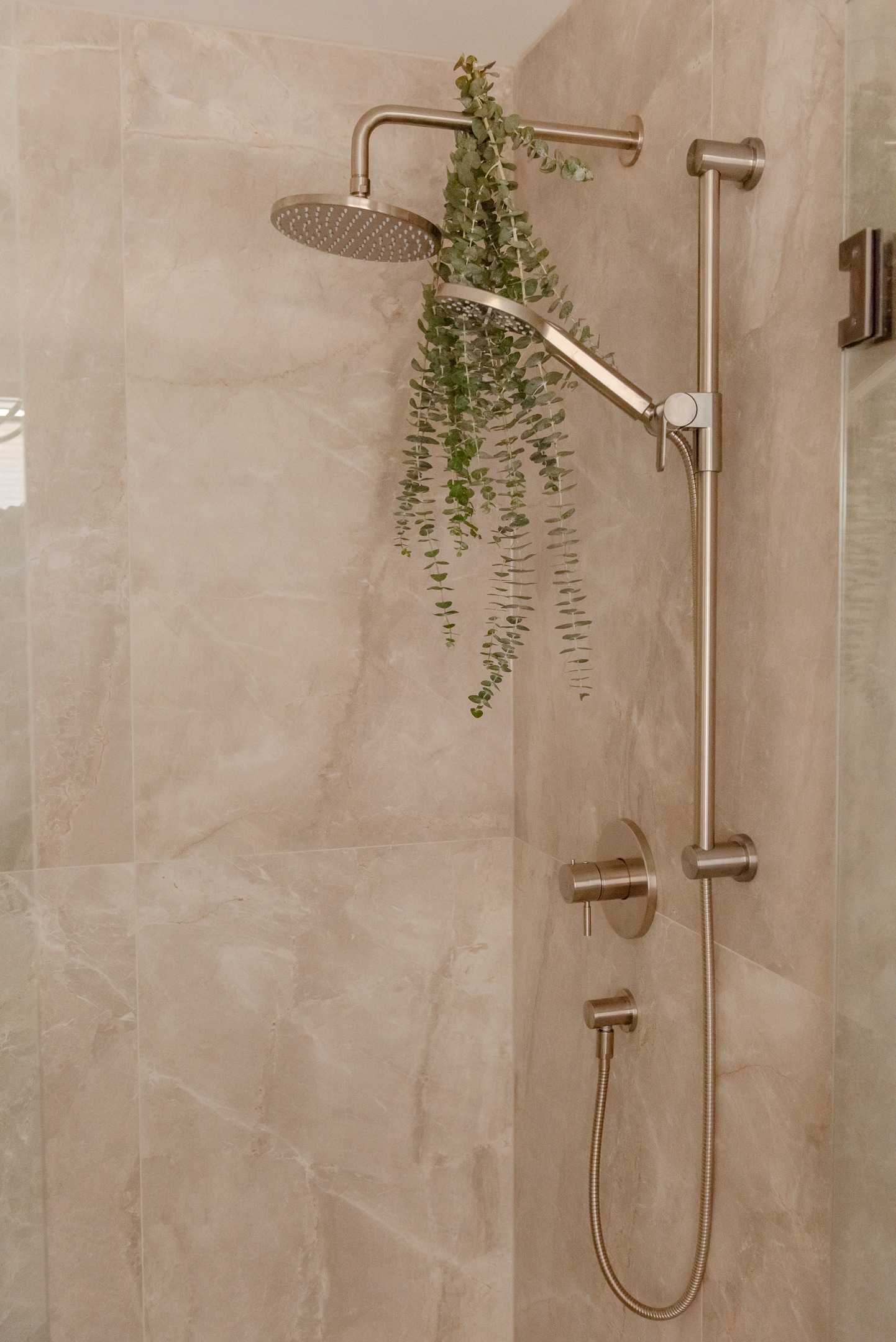 Walk-in shower featuring large-format beige stone-look tile, frameless glass enclosure and brushed metal rain shower fixtures.