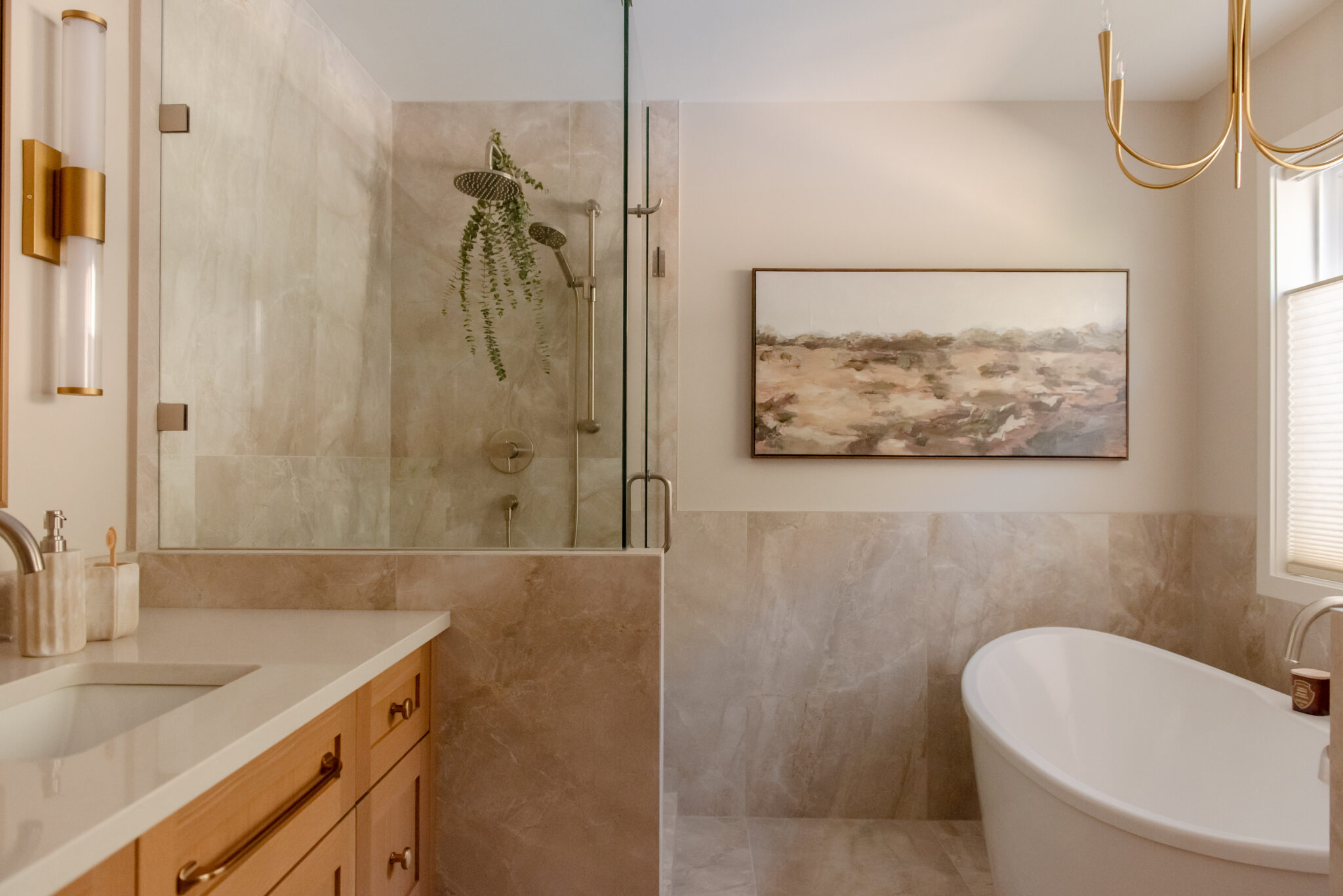 Renovated primary ensuite with warm wood double vanity, brass-framed mirror, wall sconces and glass walk-in shower.