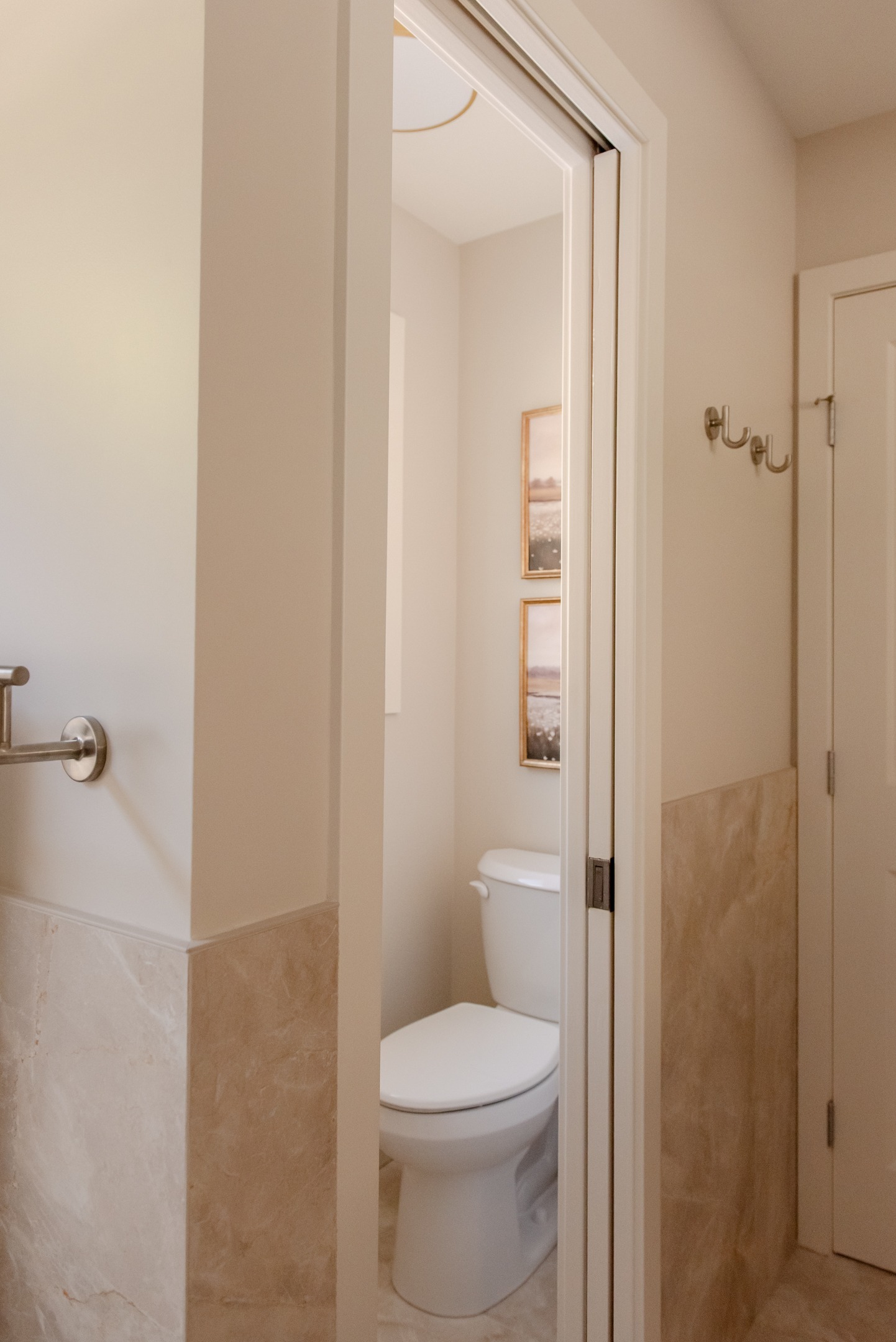 Renovated water closet in primary ensuite with beige stone look tile wainscotting