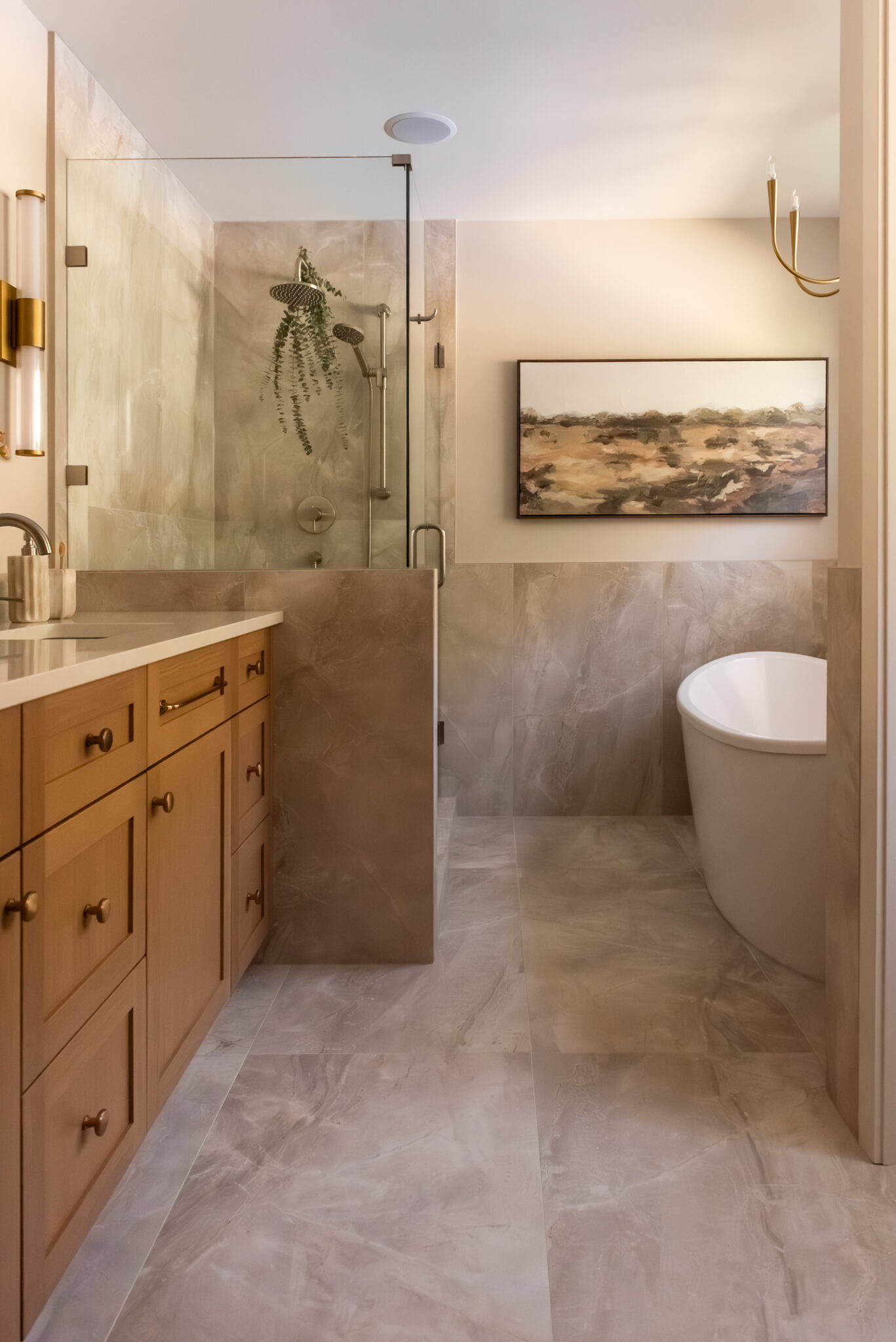 Renovated primary ensuite with warm wood double vanity, brass-framed mirror, wall sconces and glass walk-in shower.