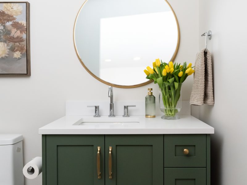 basement bathroom with green vanity and round mirror and tulips