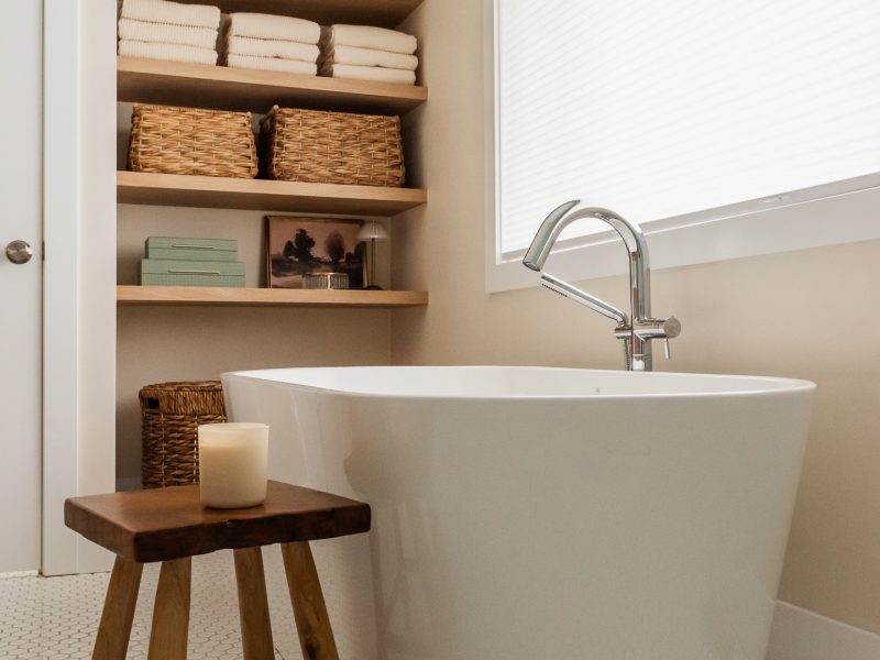 transitional primary ensuite, warm wood tones and white tile, stand alone tub under window