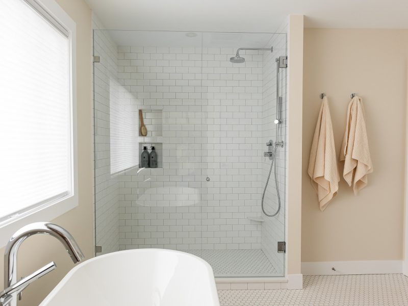 transitional primary ensuite, warm wood tones and white tile, stand alone tub, walk in shower