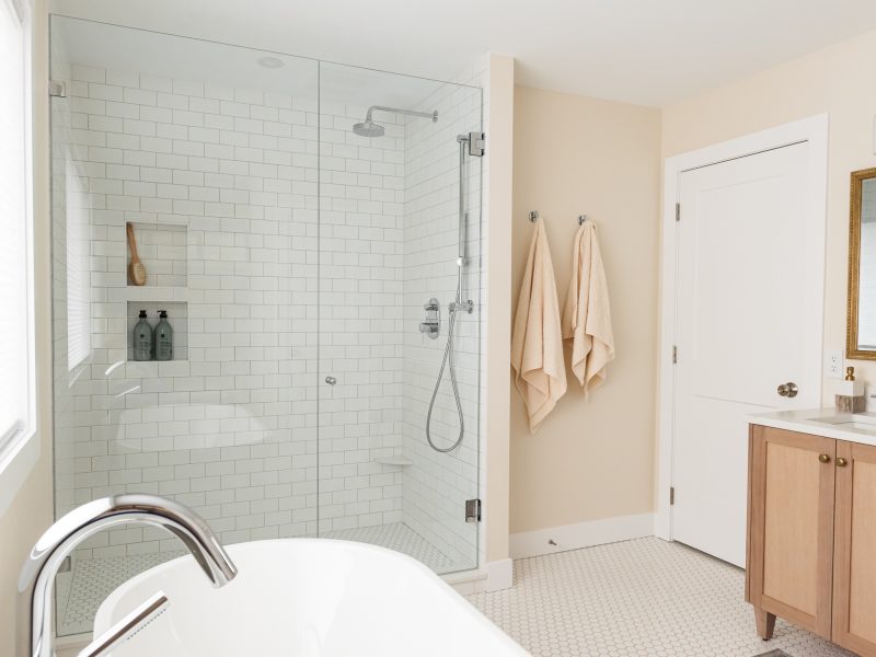 transitional primary ensuite, warm wood tones and white tile, stand alone tub, walk in shower