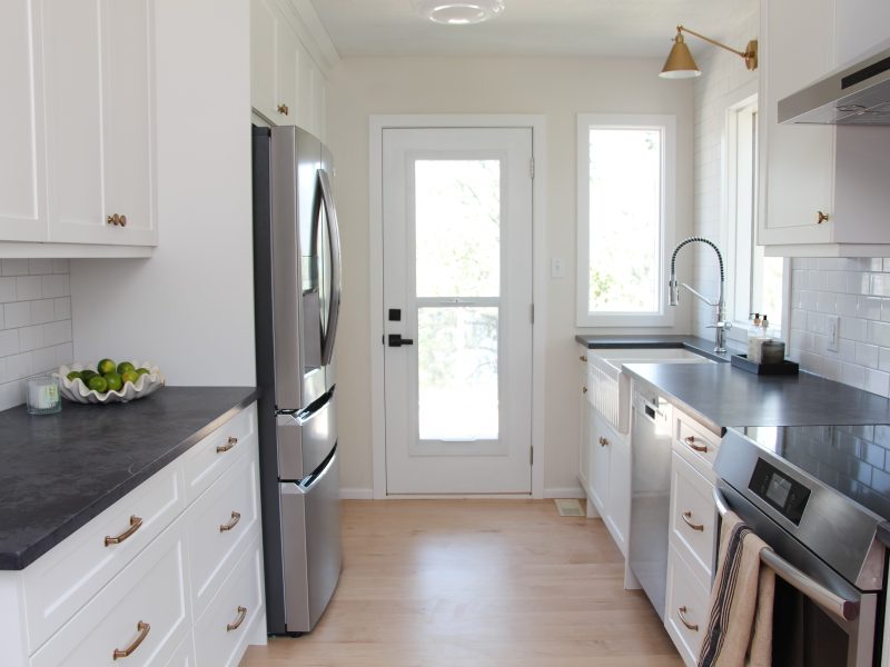 white galley kitchen with black quartz countertop, farmhouse sink, gold hardware