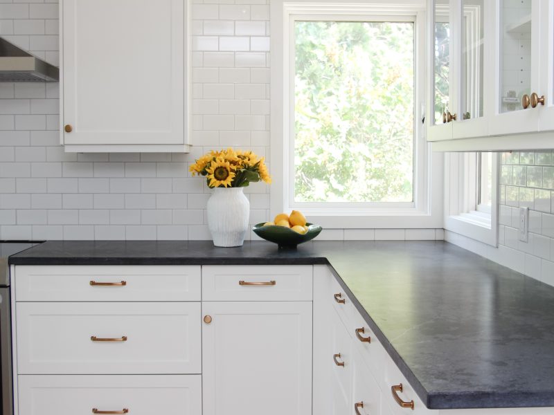timeless white kitchen cabinets, black quartz counter, gold sconce over window, sunflowers and lemon decor, subway tile to ceiling