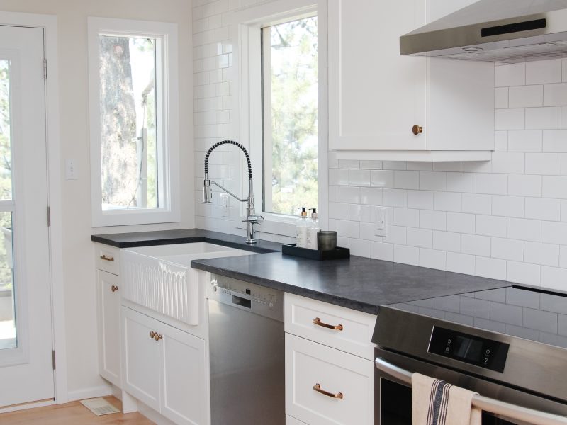 white galley kitchen with black quartz countertop, farmhouse sink, gold hardware